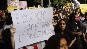 Jovens em uma manifestação carregando um cartaz com os dizeres: "Educação não é gasto, é investimeno"